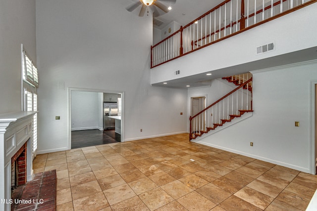 unfurnished living room with ceiling fan, a high ceiling, and a brick fireplace