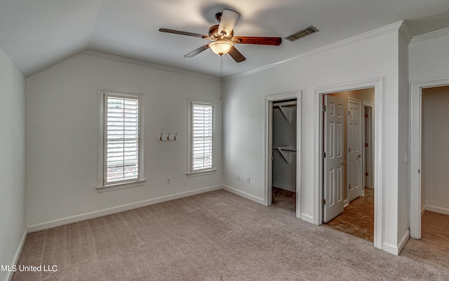 unfurnished bedroom featuring a walk in closet, ceiling fan, vaulted ceiling, ornamental molding, and light colored carpet