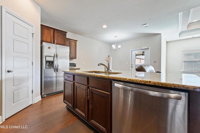 kitchen featuring appliances with stainless steel finishes, dark wood-style flooring, light stone countertops, pendant lighting, and a sink