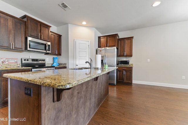 kitchen with appliances with stainless steel finishes, a kitchen breakfast bar, light stone countertops, a kitchen island with sink, and a sink