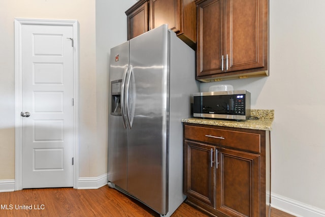 kitchen featuring stainless steel appliances, dark wood-type flooring, light stone counters, and baseboards