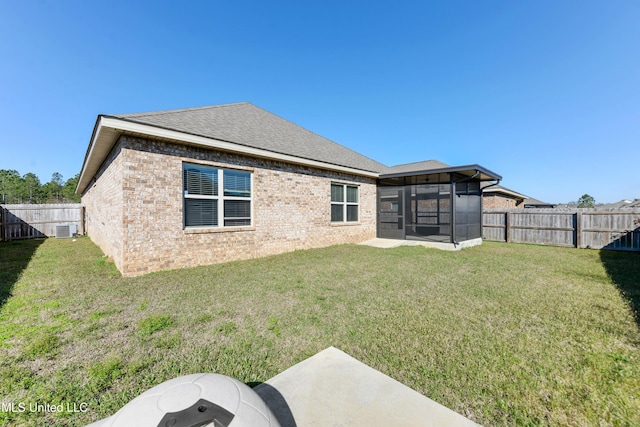 back of house with brick siding, a lawn, a fenced backyard, and a sunroom