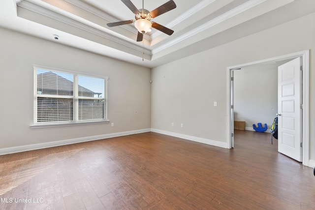 empty room with crown molding, a tray ceiling, dark wood-type flooring, and baseboards