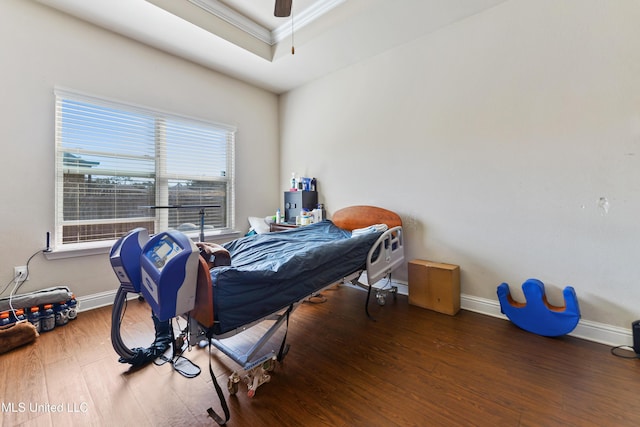 bedroom featuring ornamental molding, a tray ceiling, baseboards, and wood finished floors