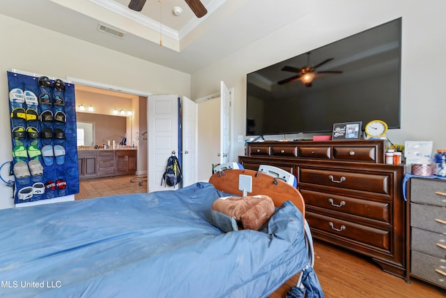 bedroom featuring visible vents, a ceiling fan, ensuite bath, crown molding, and light wood-style floors