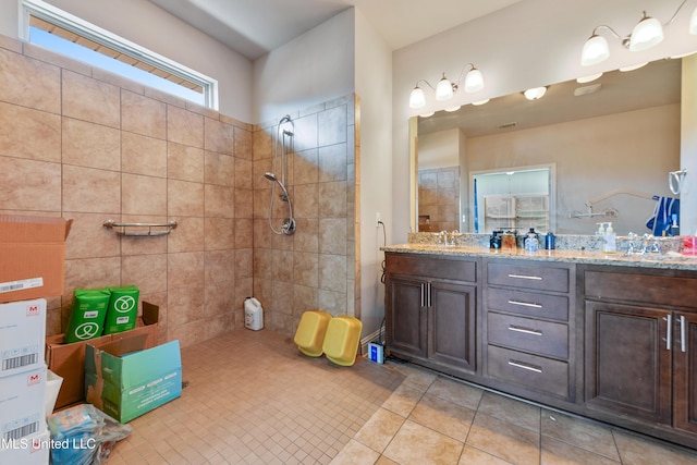 full bath with double vanity, tile patterned flooring, a tile shower, and a sink