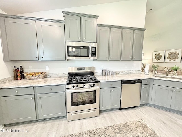 14007 Plantation Oaks Dr, Gulfport, MS 39503 - kitchen with appliances with stainless steel finishes, gray cabinets, a sink, vaulted ceiling, and light wood-type flooring