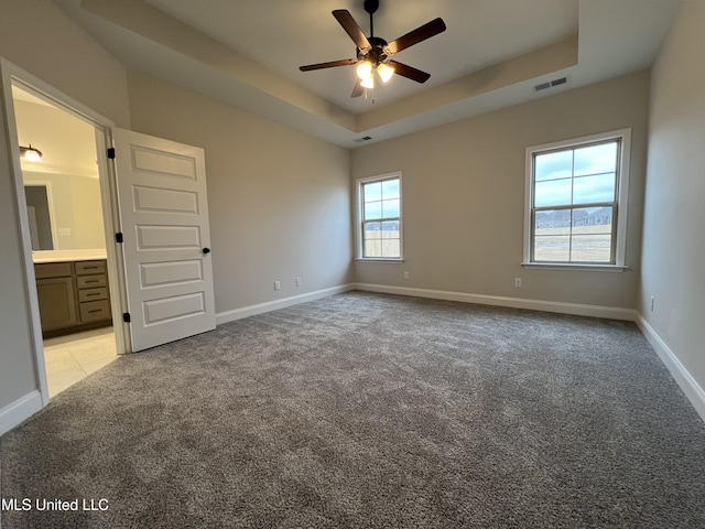 unfurnished bedroom featuring baseboards, a raised ceiling, visible vents, and light colored carpet