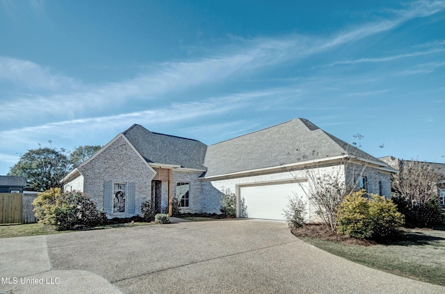 french country style house featuring an attached garage, brick siding, fence, concrete driveway, and roof with shingles