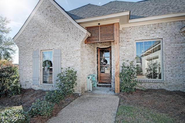 view of exterior entry featuring a shingled roof and brick siding