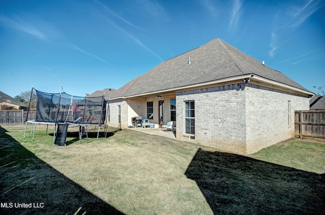 rear view of house with a trampoline, brick siding, a yard, fence, and ceiling fan