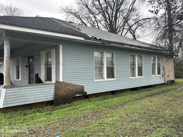 view of side of home with covered porch and a yard