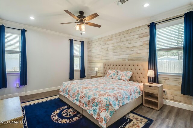 bedroom with wooden walls, wood finished floors, baseboards, visible vents, and ornamental molding