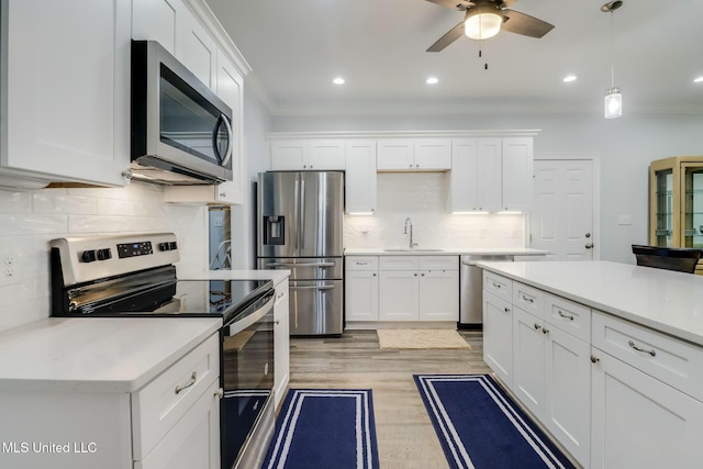 kitchen with white cabinets, stainless steel appliances, crown molding, and a sink