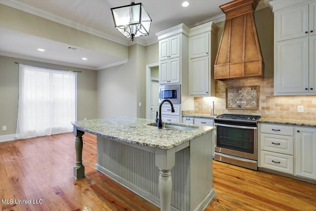 kitchen featuring appliances with stainless steel finishes, custom range hood, sink, white cabinets, and hanging light fixtures