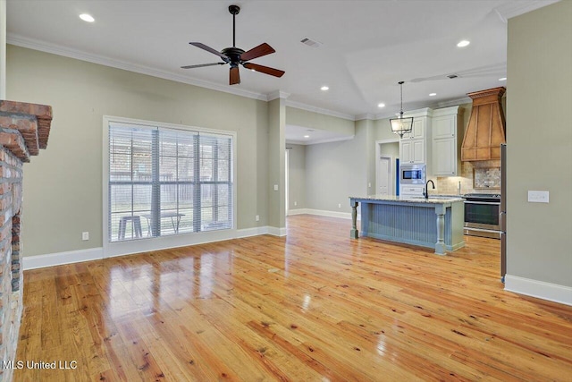 kitchen with pendant lighting, decorative backsplash, ornamental molding, an island with sink, and stainless steel appliances