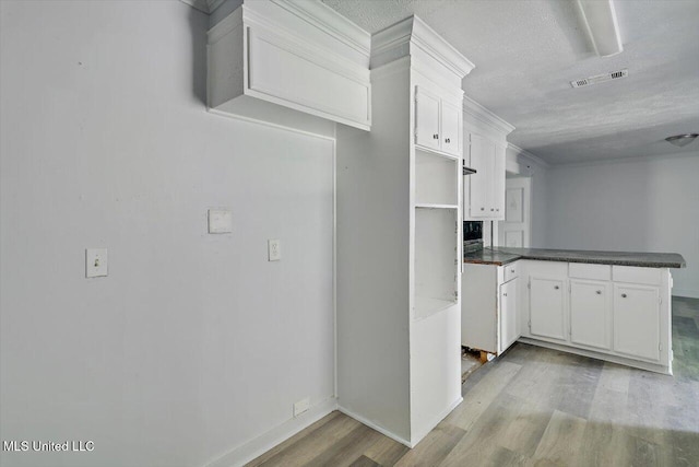 kitchen featuring light wood-style floors, a peninsula, white cabinetry, a textured ceiling, and dark countertops