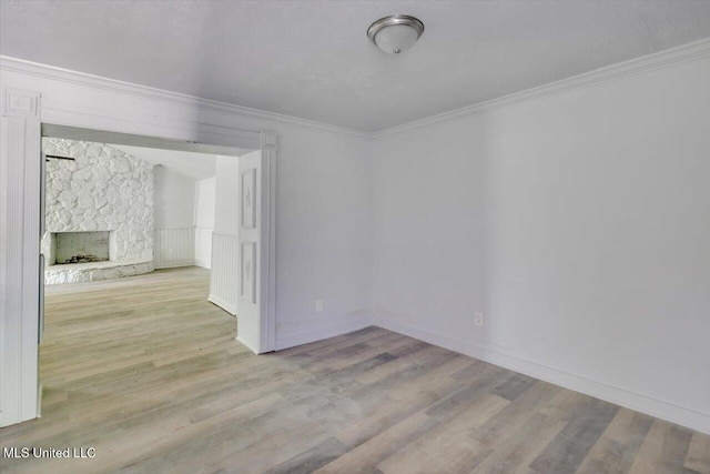 unfurnished room with wood finished floors, ornamental molding, and a stone fireplace
