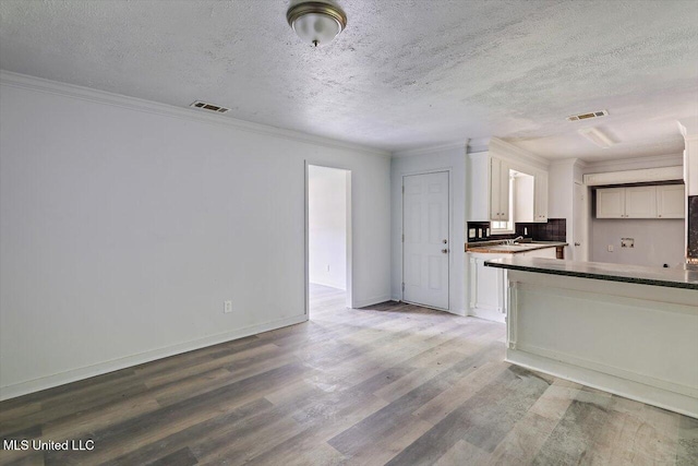 kitchen with wood finished floors, dark countertops, white cabinetry, ornamental molding, and a textured ceiling