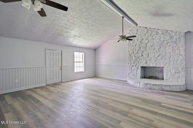 unfurnished living room featuring a ceiling fan, a textured ceiling, wood finished floors, and a fireplace