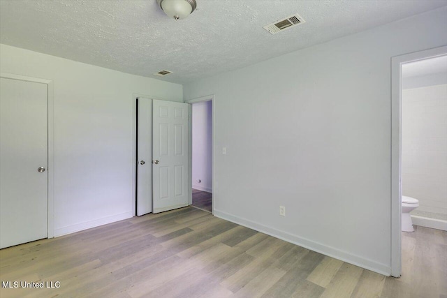 unfurnished bedroom featuring wood finished floors, a textured ceiling, baseboards, a closet, and ensuite bathroom
