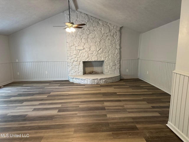 unfurnished living room with lofted ceiling, a ceiling fan, wainscoting, wood finished floors, and a stone fireplace