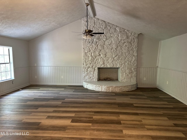 unfurnished living room with ceiling fan, wood finished floors, wainscoting, a stone fireplace, and a textured ceiling