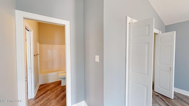 bathroom featuring hardwood / wood-style flooring, washtub / shower combination, and toilet