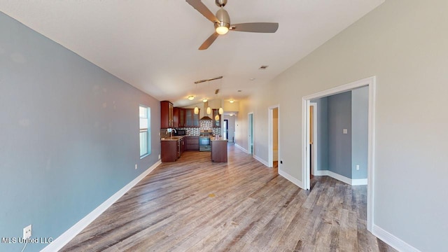 kitchen with vaulted ceiling, stainless steel stove, wood-type flooring, ceiling fan, and wall chimney exhaust hood