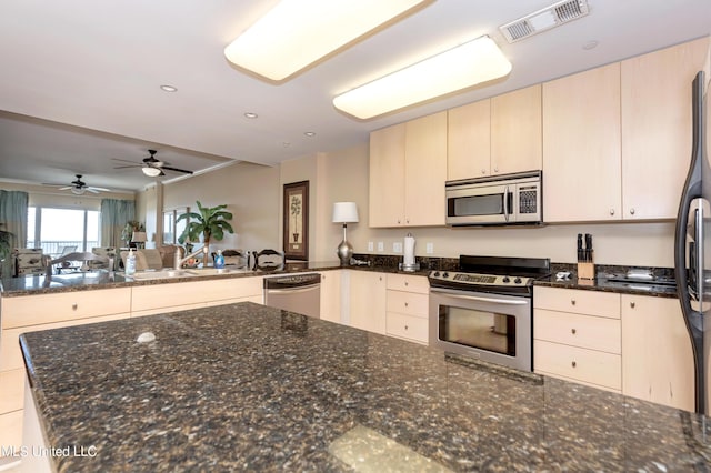 kitchen featuring kitchen peninsula, appliances with stainless steel finishes, ceiling fan, and dark stone countertops