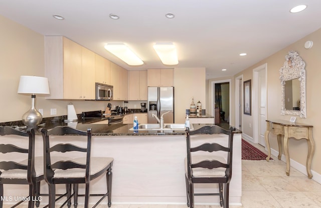 kitchen with stainless steel appliances, kitchen peninsula, dark stone countertops, cream cabinets, and a breakfast bar area