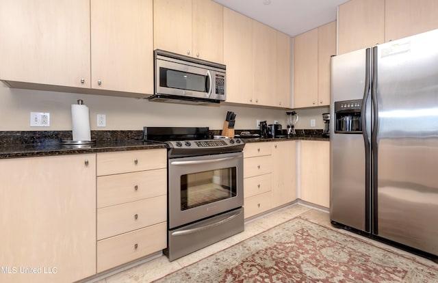 kitchen featuring light brown cabinets, dark stone countertops, and stainless steel appliances