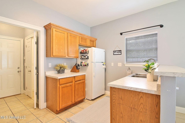 kitchen featuring baseboards, light tile patterned flooring, freestanding refrigerator, a sink, and light countertops