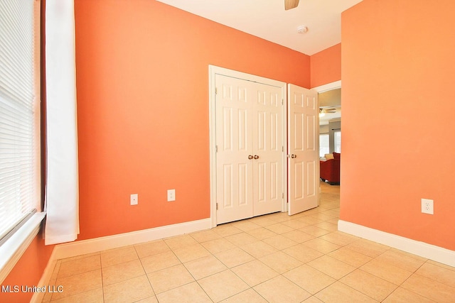 unfurnished bedroom with light tile patterned floors, baseboards, a closet, and ceiling fan