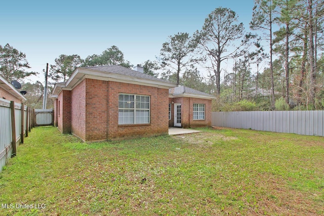 rear view of property with a chimney, a fenced backyard, brick siding, and a lawn