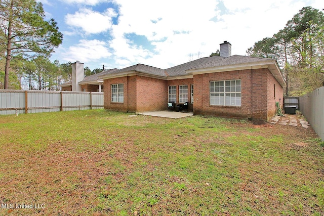 rear view of property featuring a lawn, a fenced backyard, brick siding, a chimney, and a patio area