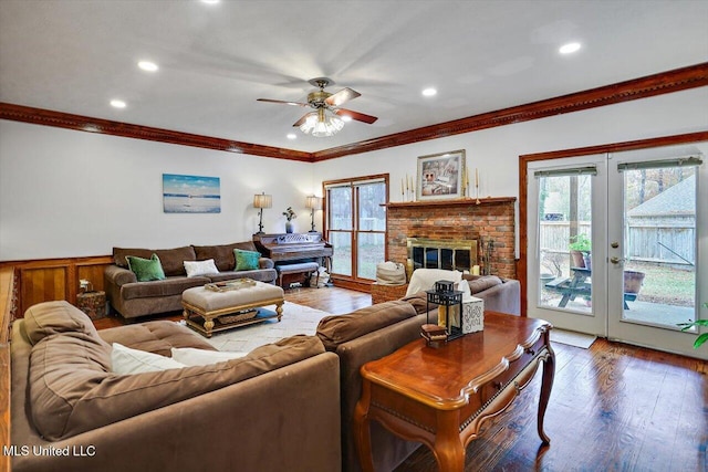 living room featuring french doors, a brick fireplace, ceiling fan, crown molding, and wood-type flooring