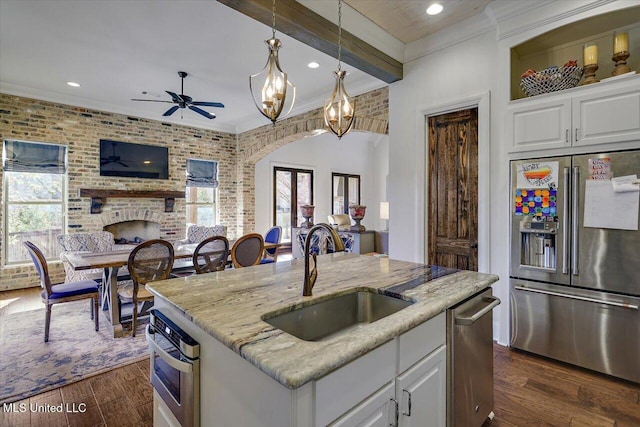 kitchen featuring white cabinetry, light stone counters, stainless steel appliances, and a center island with sink