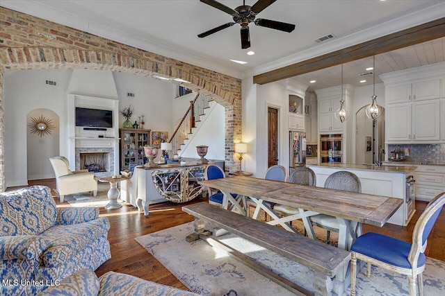 dining space featuring sink, crown molding, dark wood-type flooring, ceiling fan, and brick wall