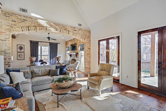 living room with hardwood / wood-style floors, high vaulted ceiling, a fireplace, brick wall, and french doors