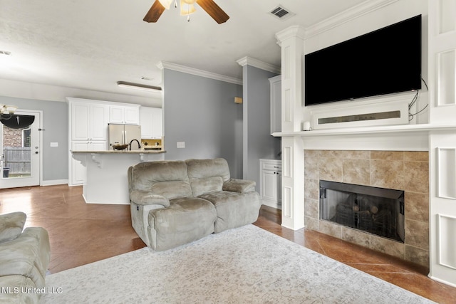 living area with crown molding, baseboards, visible vents, and ceiling fan