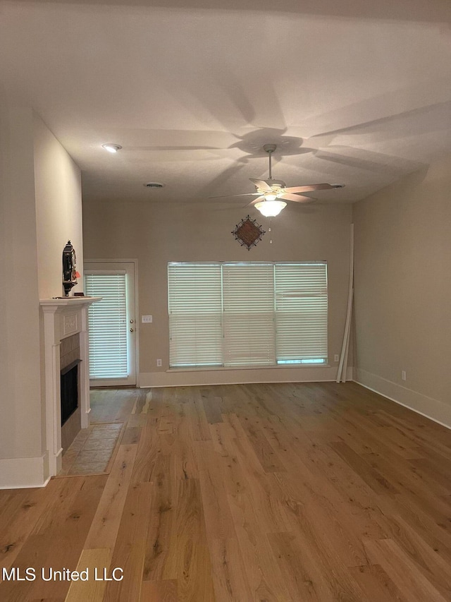 unfurnished living room with hardwood / wood-style flooring, a tiled fireplace, and ceiling fan