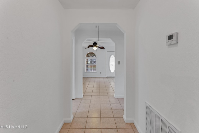 corridor with visible vents, arched walkways, baseboards, and light tile patterned floors