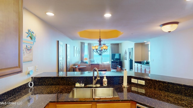 kitchen with sink, dark stone countertops, hanging light fixtures, a raised ceiling, and a notable chandelier