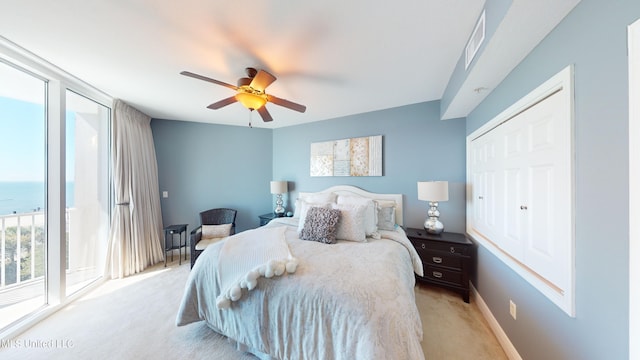 bedroom with a closet, access to exterior, a water view, light colored carpet, and ceiling fan