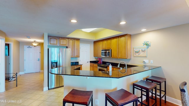 kitchen with stainless steel appliances, dark stone counters, a kitchen bar, sink, and kitchen peninsula