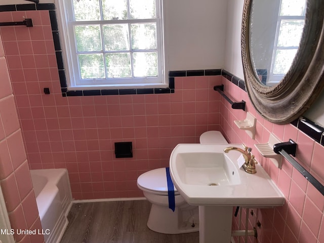 bathroom with a bathing tub, hardwood / wood-style flooring, toilet, and tile walls