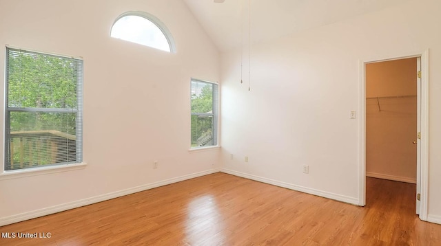 spare room featuring light wood-style floors, baseboards, and high vaulted ceiling