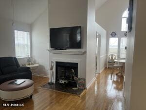 living room with high vaulted ceiling, a fireplace, wood finished floors, and baseboards