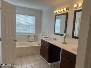 full bathroom featuring double vanity, tile patterned floors, a garden tub, crown molding, and a sink